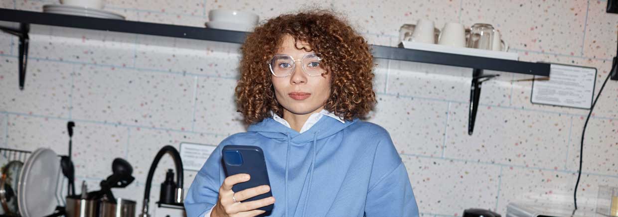 frau mit locken haelt smartphone in moderner kueche